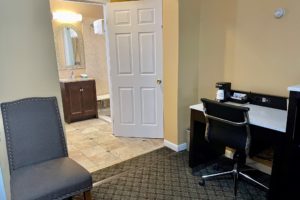 Desk with coffee maker, office chair, chair, doorway to bathroom with vanity unit, mirror, tiled and carpet flooring