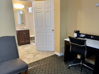 Desk with coffee maker, office chair, chair, doorway to bathroom with vanity unit, mirror, tiled and carpet flooring