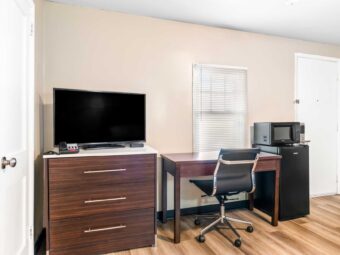 Wooden drawer unit with TV, desk with chair, fridge with microwave, laminate flooring