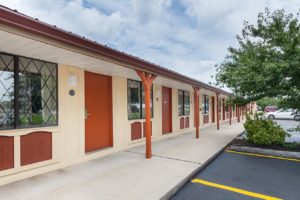 One story building with exterior room entrances, parking spaces, small trees and bushes