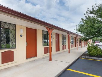 One story building with exterior room entrances, parking spaces, small trees and bushes