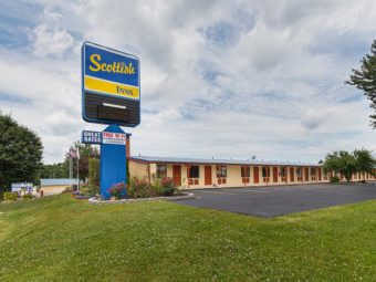 Brand signage, one story building with exterior room entrances, flower beds, grassy area, parking spaces