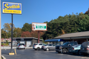 Hotel entrance, one story building, parking spaces, brand signage, large trees behind hotel,