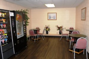 Vending machines with snacks and drinks, small tables and chairs, art images, potted plants, vases with flowers, laminate flooring