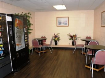 Vending machines with snacks and drinks, small tables and chairs, art images, potted plants, vases with flowers, laminate flooring