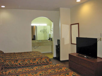 Two queen beds, wooden unit with flat screen tv, wall mounted mirror, fridge with microwave, archway to vanity unit with wall mounted towel rail with towels, wall mounted hanging rail and mirror with overhead strip light, laminate flooring