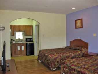 Two queen beds, night stand, wall mounted art, wooden unit with flat screen tv, laminate flooring, archway to kitchenette with cabinetry, fridge , coffee maker and microwave