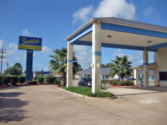 Hotel entrance with drive through canopy, brand signage, landscape flower beds and trees