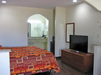 King bed, wooden unit with fkat screen tv, wall mounted mirror, fridge and microwave, archway to vanity unit with hangingin rail, towel rail with towels, wall mounted mirror, coffee maker, laminate flooring