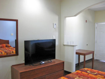 King bed, wooden unit with flat screen tv, small table, laminate flooring