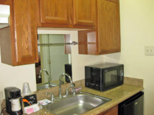 Kitchentte with wall and base cupboards, counter top with sink, microwave and coffee maker, fridge