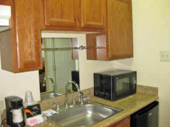 Kitchentte with wall and base cupboards, counter top with sink, microwave and coffee maker, fridge