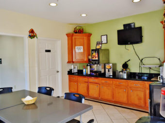 Breakfast display area with coffee machine, waffle machine, wall mounted flatscreen TV, fridge, table and chairs, tiled flooring