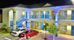 Two story building at night with exterior room entrances, walkways and stairs, aprking spaces, landscaped beds with small bushes and trees, parking spaces