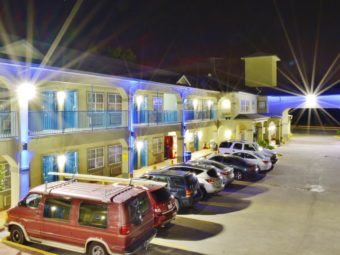 Two story building displayed with night time lighting showing exterior room entrances, walkways, parking spaces