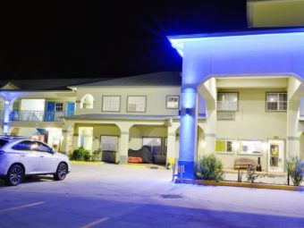 Hotel entrance displaying night time lighting with drive through canopy, small landscaping beds with bushes, parking spaces