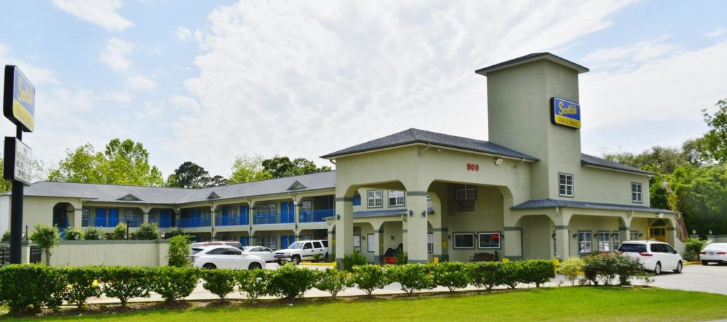 Hotel entrance with drive through canopy, two story building with exterior room entrances, walkways and stairs, parking spaces, grassy area with small bushes