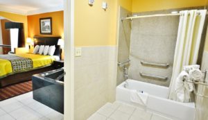 Shower Tub with grab handles, shower curtain, towel rack with towels, tiled flooring, doorway to bedroom with king bed