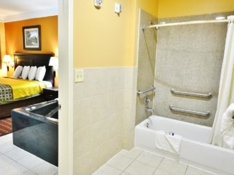 Shower Tub with grab handles, shower curtain, towel rack with towels, tiled flooring, doorway to bedroom with king bed