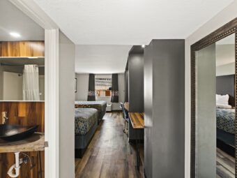 Large mirror, desk, office chair, two queen beds, laminae flooring, doorway to bathroom with backlit mirror, vanity unit