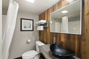 Backlit mirror, vanity unit, toilet, shelf and hanging rail with towels, shower tub with shower curtain