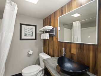Backlit mirror, vanity unit, toilet, shelf and hanging rail with towels, shower tub with shower curtain