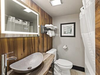 Backlit mirror, vanity unit, toilet, shelf and hanging rail with towels, shower tub with shower curtain, tiled flooring