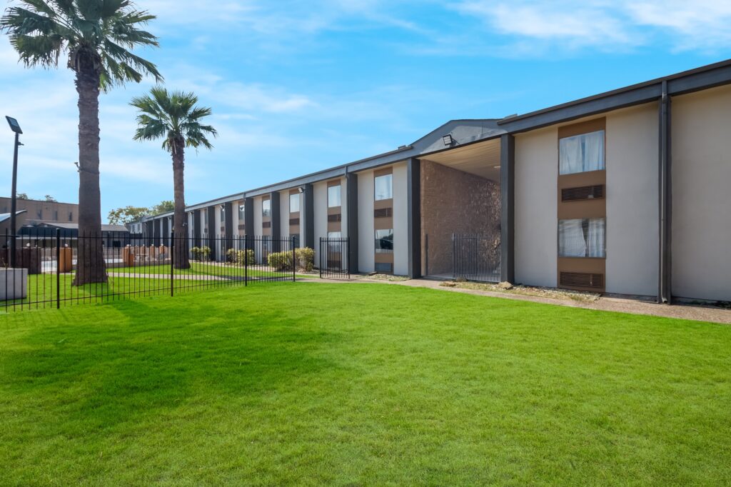 STXAU Exterior 101 Two story building, metal fencing, outdoor pool with fencing, grassy area, palm trees