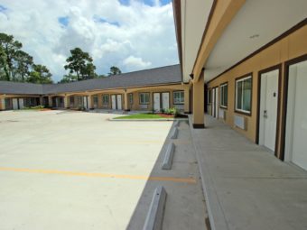 One story building with exterior room entrances and covered walk way, parking spaces, landscaping with shrubs and grass