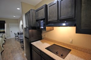 kitchenette area with base and wall cabinets, counter top with hob, laminate flooring, two queen beds, desk with chair, small table with chair, wall mounted flat screen tv