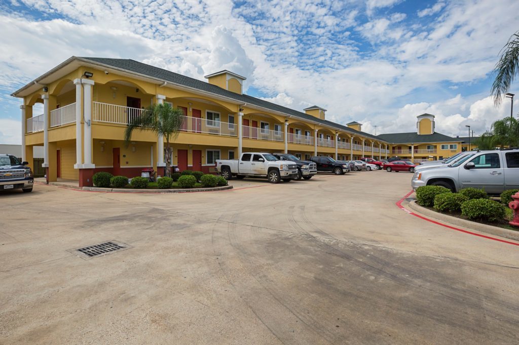 STXBT Exterior 1 Two story building with exterior room entrances, covered walkways, parking spaces, landscaping with small bushes and trees