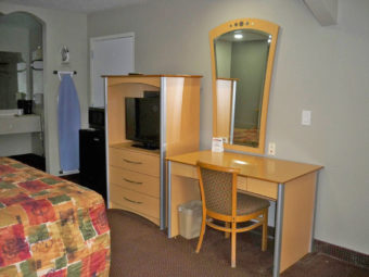 Desk with chair, wall mounted mirror, wooden tv console unit with flat screen tv, fridge, microwave, wall mounted ironing board and iron, king bed, carpet flooring, alcove with vanity unit, coffee maker and wall mounted mirror