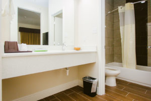 Vanity Unit, mirror, towel rail with towels, doorway to bathroom, shower tub with shower curtian, toilet, tiled flooring