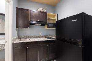 counter top with sink and hob, base and wall cabinets with microwave, fridge, doorway to bathroom