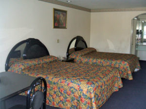 Two queen beds, night stand with telephone, small table and chairs, carpet flooring, alcove with vanity unit and mirror