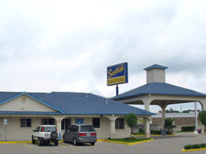 Hotel entrance with canopy drive through, one story guilding, parking spaces, brand signage