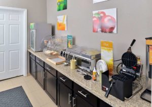 Breakfast counter display with small chilled cabinet, breakfast pastries display case, hot self serve food containers, waffle machine, wall mounted art, tiled flooring