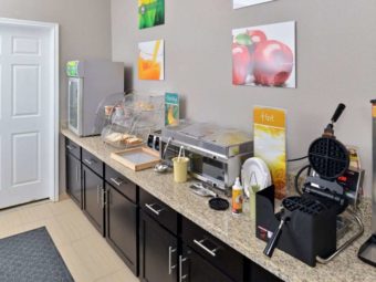 Breakfast counter display with small chilled cabinet, breakfast pastries display case, hot self serve food containers, waffle machine, wall mounted art, tiled flooring