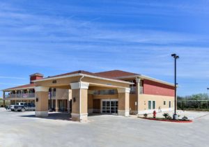 Two story building with exterior walkways, hotel canopy entrance, parking spaces