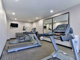 Fitness machines, wall mounted flat screen tv, sofa, weights, metal shelving with towels, large wall mounted mirrors, carpet flooring