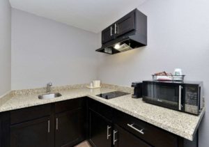 base cabinets with granite counter top, sink, ice bucket, hob unit, cooker hood with overhead cabinets, coffee maker and microwave