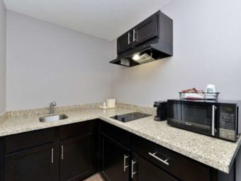 base cabinets with granite counter top, sink, ice bucket, hob unit, cooker hood with overhead cabinets, coffee maker and microwave