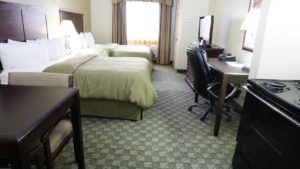 Two queen beds, stove, small table and chair, desk with office chair and telephone, wooden drawer unit with flat screen tv, carpet flooring