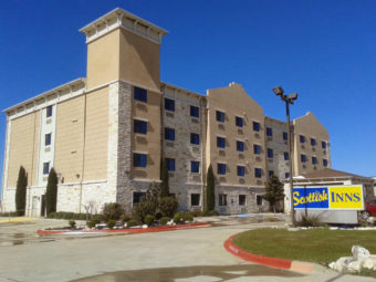 Hotel Entrance, brand signage, four story building, landscaping with grassy areas, shrubs and small trees