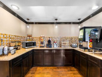 Counter with disposable plates and silverware, cereal dispensers, microwave with fruit basket, waffle mixture dispenser, waffle machine, bread display cabinet, toaster, juice machine, coffee machine