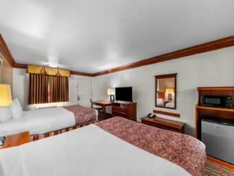 Two queen beds, night stand with bedside lamp, art images, desk with chair and lamp, wooden drawer unit with flatscreen TV, mirror, wooden bench with telephone, wooden unit with microwave and fridge, carpet flooring
