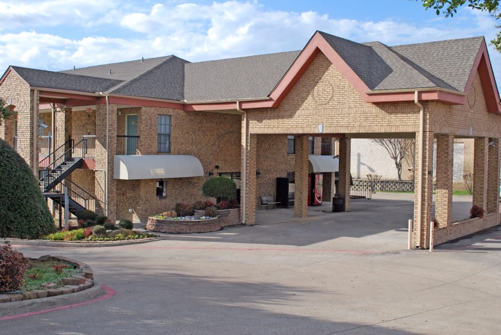 Entrance with drive through canopy, flower beds, small shrubs, vending machine, exterior stairs to upper level