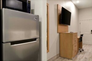Full size fridge with microwave, wooden drawer unit, wall mounted TV, desk with office chair, laminate flooring