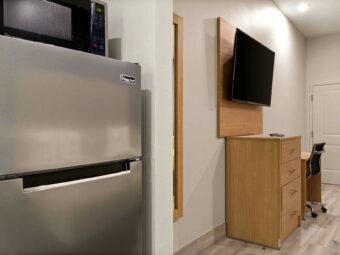 Full size fridge with microwave, wooden drawer unit, wall mounted TV, desk with office chair, laminate flooring