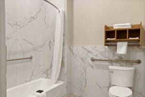 Shower tub with grab handles, bath mat and shower curtain, toilet with grab handle, shelves with towels